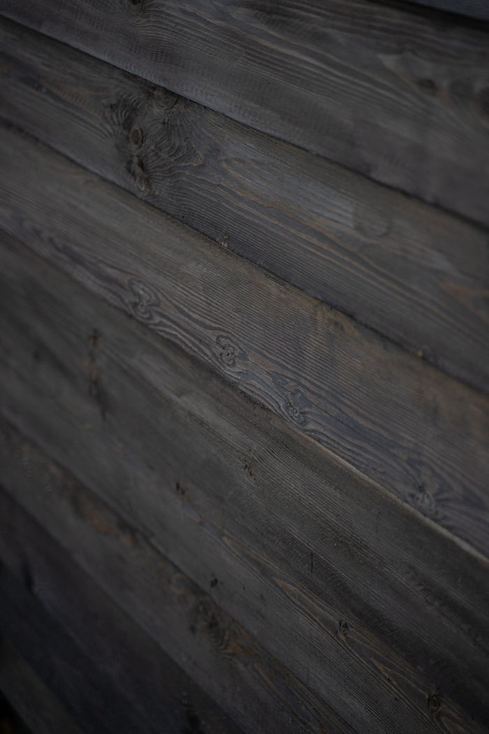 Close-up of a dark wooden wall with a rough, rustic texture and weathered appearance.