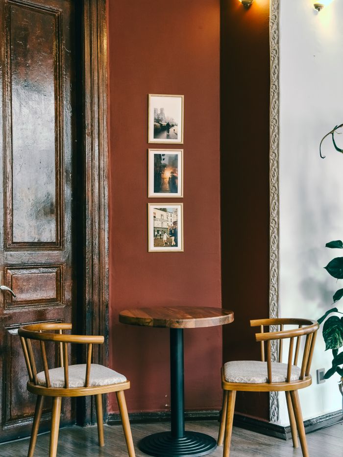 Charming cafe interior with wooden chairs and table against a red feature wall with framed photos.